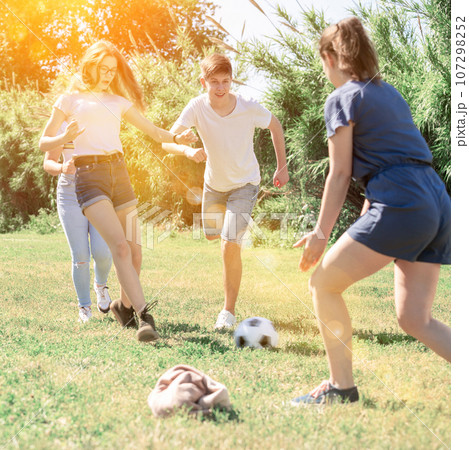 Teenagers playing football on green grass in summertime Teenagers playing football on green grass in summertime 107298252