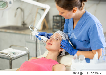 Adult woman cosmetologist doing whitening procedure to young woman 107298276