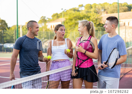 Group of four tennis players standing on court and talking friendly Group of four tennis players standing on court and talking friendly 107298282