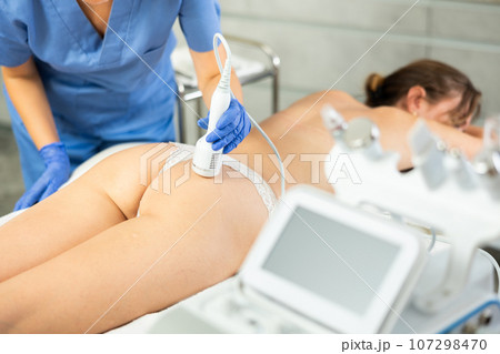 Young girl lying in spa while having body treatment procedures with technologies shrink pores and repair damaged skin. Hardware cosmetology and dermatology Young girl lying in spa while having body treatment procedures with technologies shrink pores and repair damaged skin. Hardware cosmetology and dermatology 107298470