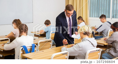 Teacher man helping students during lesson in schoolroom 107298604