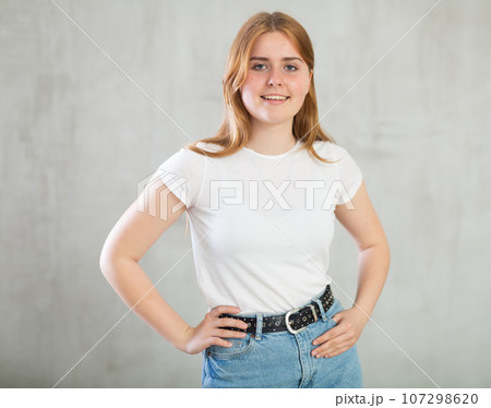 Happy smiling teenage girl, student in casual clothes looking at camera at gray wall background, copy space for mock up 107298620