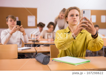 Schoolgirl using phone in classroom during lesson 107298622