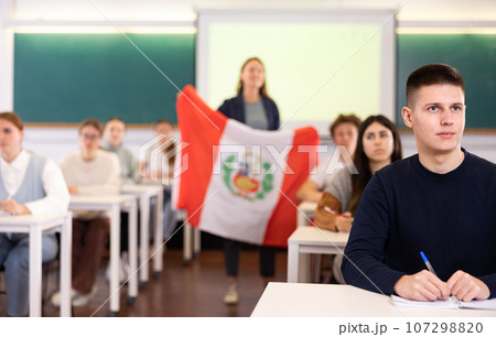 Teenage students in class and listening carefully to female teacher holding Peru flag in hands 107298820