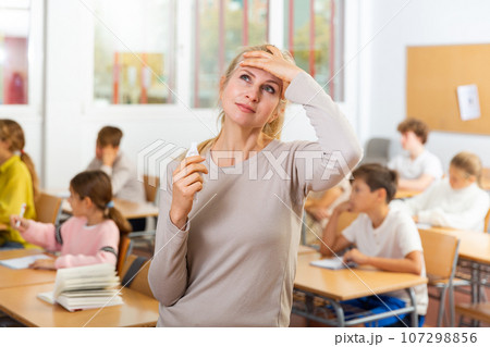 Upset female school teacher standing in classroom Upset female school teacher standing in classroom 107298856