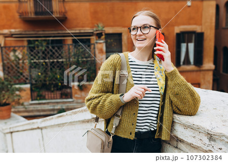 Happy young blonde woman talk phone, listen at the street. Phone Communication. Feminine gossip while relaxing on urban background, traveler 107302384