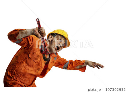 A scary construction worker zombie with blood and wounds on his body walking while carrying a pipe wrench 107302952
