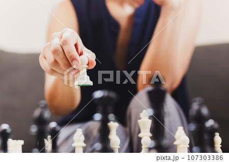 Woman playing chess board game at home. 107303386