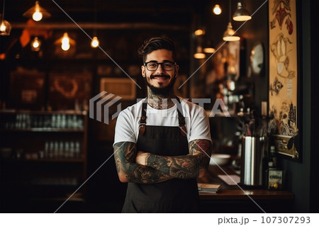 Handsome young tattooed hipster bartender in apron smiling in pub 107307293