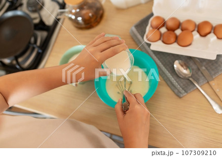 the cooking process, the woman adds milk to the pancake batter 107309210