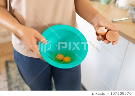 a woman breaks chicken eggs in a bowl while standing in the kitchen 107309570