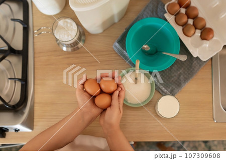 A woman holds chicken eggs in her hands while standing in the kitchen 107309608