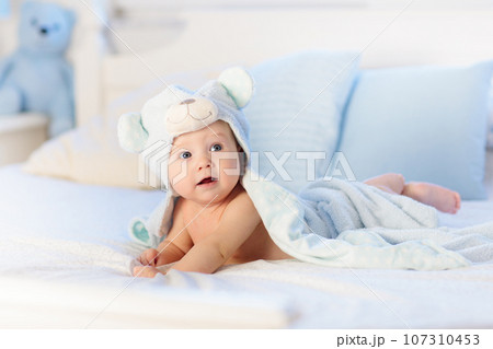 Baby boy in blue towel on white bed 107310453