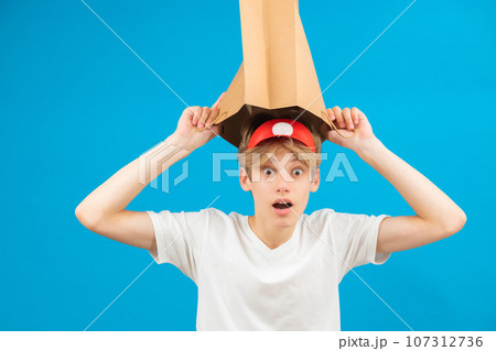 Shocked seller teen boy with paper bag over head. Teenager holding paper bag over the head posing in studio. Guy pulling paper bag over head. Shocked seller teen boy with paper bag over head. Teenager holding paper bag over the head posing in studio. Guy pulling paper bag over head. 107312736