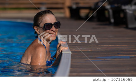 An elderly woman in sunglasses swims in the pool. Vacation in retirement.  107316069