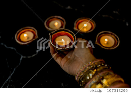 Happy Diwali - Woman hands with henna holding lit candle isolated on dark background. 107318296