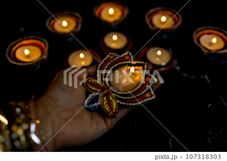 Happy Diwali - Woman hands with henna holding lit candle isolated on dark background. Happy Diwali - Woman hands with henna holding lit candle isolated on dark background. 107318303