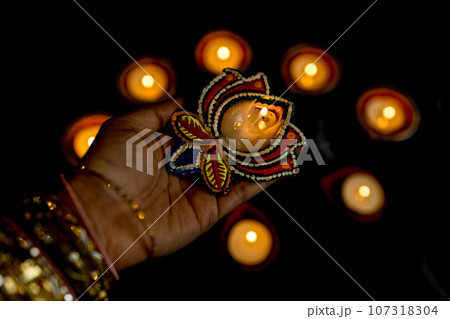 Happy Diwali - Woman hands with henna holding lit candle isolated on dark background. Happy Diwali - Woman hands with henna holding lit candle isolated on dark background. 107318304