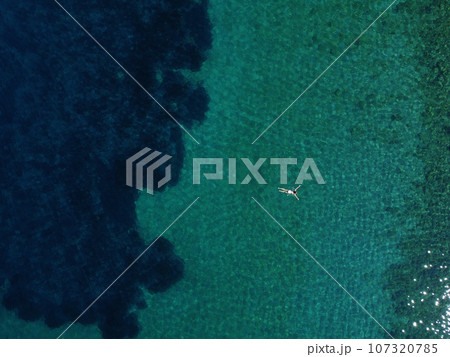 Above view of woman swimming at sea. Aerial top view of young girl in white swimsuit floating on water surface in crystal clear turquoise sea. Vacation at Paradise. Ocean relax, travel and vacation 107320785