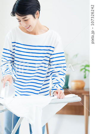 リビングでアイロン掛けする笑顔の女性 リビングでアイロン掛けする笑顔の女性 107326242