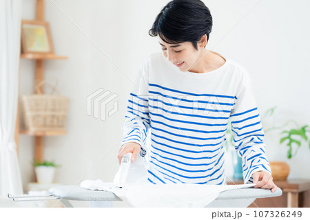 リビングでアイロン掛けする笑顔の女性 リビングでアイロン掛けする笑顔の女性 107326249