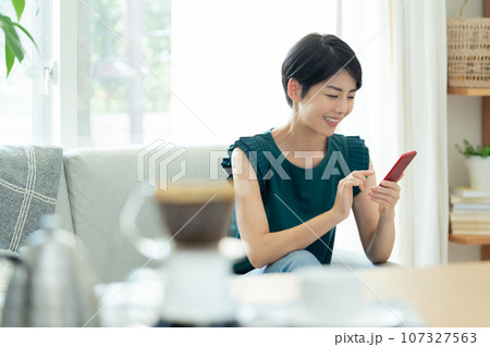 リビングでスマートフォンを操作する女性 リビングでスマートフォンを操作する女性 107327563