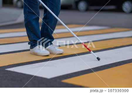 Close-up of the legs of a blind woman crossing the road at a crosswalk with a cane.  107330300