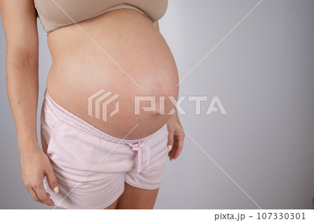 Close-up of pregnant woman's belly in third trimester on white background. Copy space.  107330301