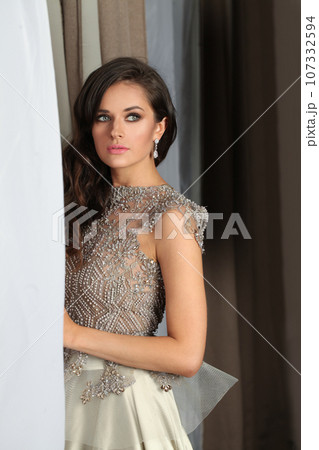 Attractive young adult woman with makeup and long wavy hairstyle posing indoor Attractive young adult woman with makeup and long wavy hairstyle posing indoor 107332594