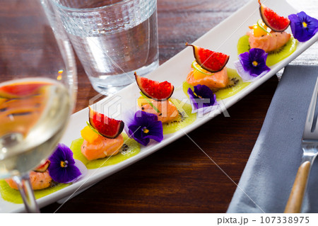 Ceviche from pickled red fish and cumquat a circle of kiwi, with figs at plate 107338975