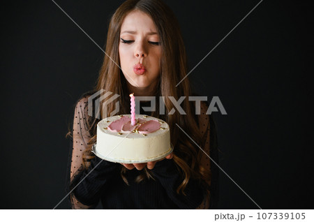 Happy teen girl wearing black dress blowing out a candle on a cake. 107339105