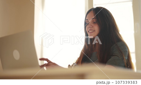 pretty girl working on a laptop at home near the window. learning students business work at home concept. girl student studying working lifestyle on a laptop near the window indoors in the classroom pretty girl working on a laptop at home near the window. learning students business work at home concept. girl student studying working lifestyle on a laptop near the window indoors in the classroom 107339383