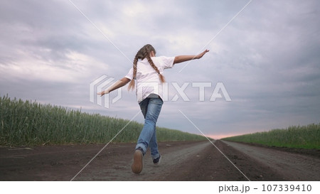 girl child running in nature in the park. happy family kid dream concept. free child daughter runs along a rural road next to a field in nature. free girl runs and plays in the park lifestyle 107339410