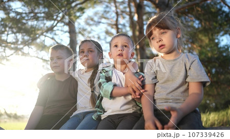a group of children plays in a forest park. group of children close-up sitting on a log of a fallen tree. happy family child dream concept. A group of lifestyle children in a pioneer camp are playing 107339426