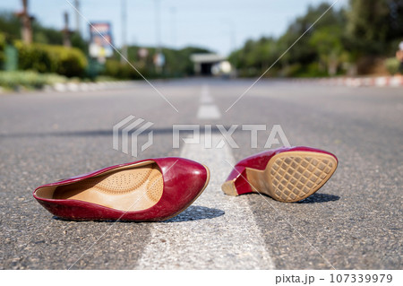 Red women's shoes lying on the road in summer day 107339979