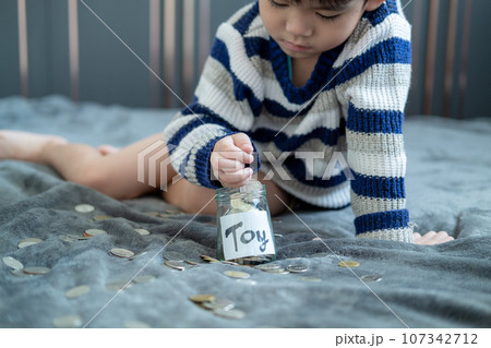 Asian boy sits and puts coins in a glass jar to save money to buy toys. 107342712