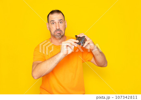 Financial crisis and bankruptcy due to the rise in prices of essential raw materials. Sad Spanish man showing empty wallet to camera, no money, spent money, yellow studio background. 107342811