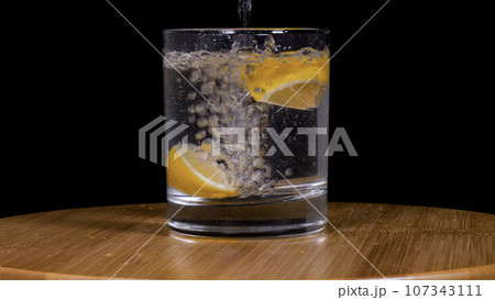 Close-up footage of soda and lemons pouring into glass on black background. 107343111