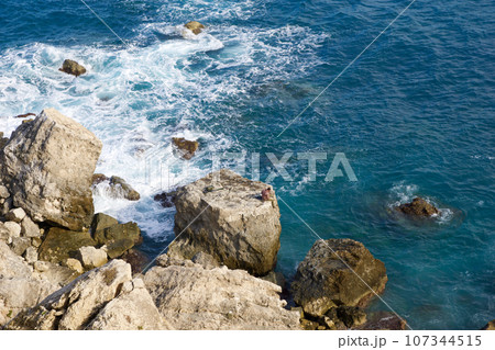 MELLIEHA, MALTA - 01 JAN, 2020: A man sitting on a rock near the ocean on the island of Malta during calm sea 107344515