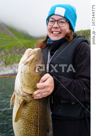 Happy young woman holding big arctic cod. Norway happy fishing. Fisherwoman with cod fish in hands Happy young woman holding big arctic cod. Norway happy fishing. Fisherwoman with cod fish in hands 107344775