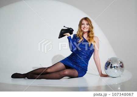 woman in shiny blue dress on floor with a disco ball on a white room 107348067