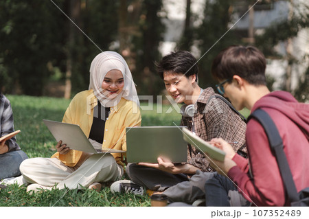 A multiethnic group of university students is studying together for an exam while sitting on the grass near the campus. A multiethnic group of university students is studying together for an exam while sitting on the grass near the campus. 107352489