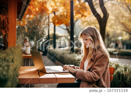 Attractive young woman working at a street cafe table on a warm autumn day 107355339