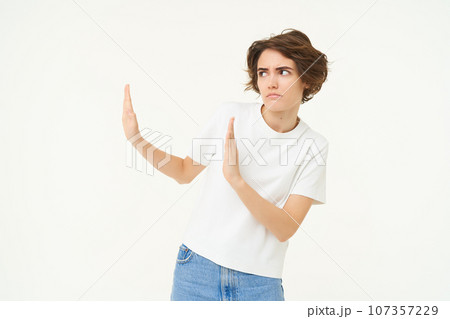 Portrait of woman avoiding someone, shows block hands gesture and refusing from something bad, standing over white background Portrait of woman avoiding someone, shows block hands gesture and refusing from something bad, standing over white background 107357229
