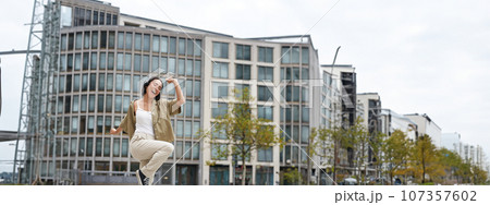 Vertical shot of dancing girl in headphones, listening music on street, enjoying sound in earphones 107357602