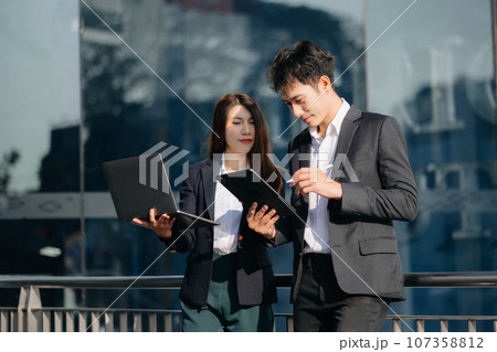 Businesswoman and woman going in city center in smart casual business style, talking, working together, stylish freelance people, laptop,tablet and smartphone 107358812