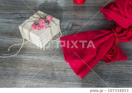 Red Santa Claus bag and gift packed in craft packaging on a wooden surface background. Red Santa Claus bag and gift packed in craft packaging on a wooden surface background. 107358853