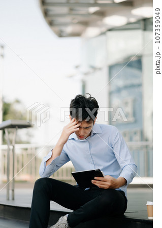 Frustrated young Asian businessman working on a laptop computer sitting at his working place in office Frustrated young Asian businessman working on a laptop computer sitting at his working place in office 107359049
