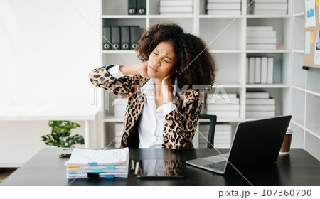 Overworked young African businesswoman office worker suffering from neck pain after had a long day at her office desk. .. Overworked young African businesswoman office worker suffering from neck pain after had a long day at her office desk. .. 107360700