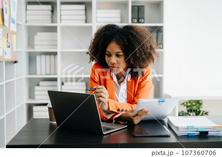 Young African woman typing on tablet and laptop while sitting at the working black table office.. Young African woman typing on tablet and laptop while sitting at the working black table office.. 107360706